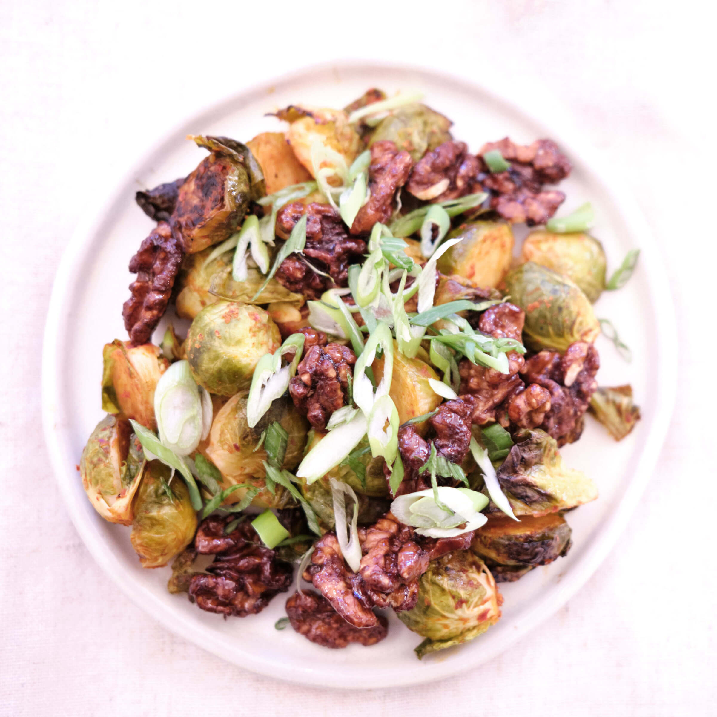 Plate of roasted brussels sprouts with kimchi paste, Acacia Honey, scallions, and Caramelized Walnuts